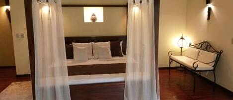 A bedroom with a bed, white curtains, a bedside lamp, and a bench.