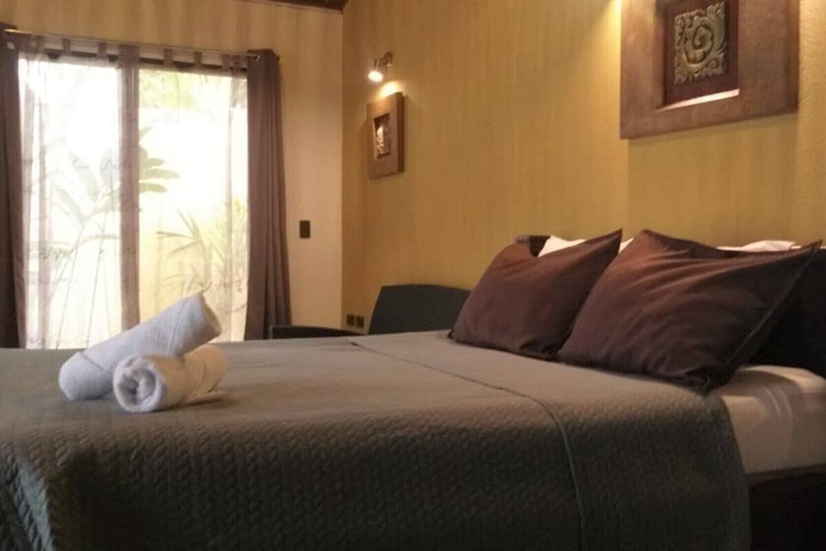 A hotel room with a bed, a chair, a window with curtains, and a wall-mounted picture.