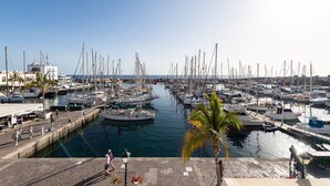 Un puerto deportivo con numerosas embarcaciones amarradas, cielo despejado y algunas personas caminando por el muelle.