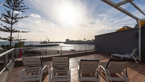 En terrasse med fire hvide liggestole, havudsigt og en klar himmel.