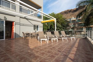 A sunlit outdoor patio with a dining table and chairs, a covered seating area, and a view of a mountainous landscape. - Gran Canaria Stays - Holiday Rentals (Mogán)