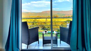 A balcony with two wicker chairs and a table, overlooking a scenic landscape with mountains and fields. - 🏅 Mediterranean Beach Style Villa with Private Pool & Jacuzzi (Tocaima)