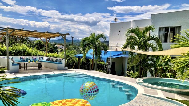 A swimming pool with a tiled deck, a lounge area with a sofa and a table, and a pergola. - 🏅 Mediterranean Beach Style Villa with Private Pool & Jacuzzi (Tocaima)
