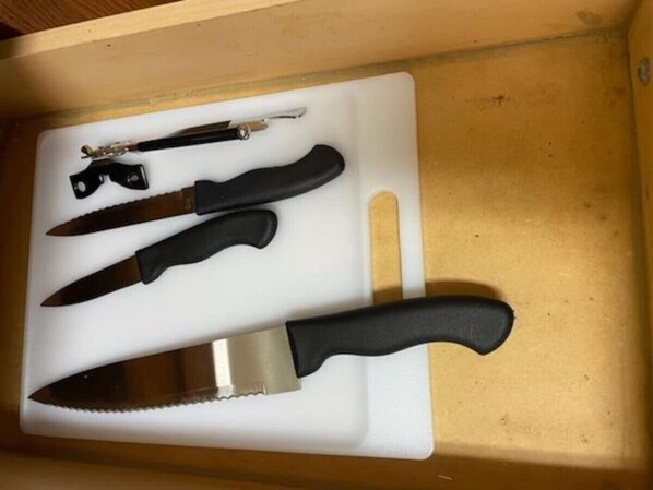 Un tiroir contenant une planche à découper blanche, un couteau à manche noir et un petit outil en métal.