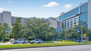 A modern building with a glass facade, a sign for 'Ochsner', and a pedestrian crossing. - Safe NOLA-steps to Ochsner hospital! (Jefferson)