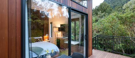 Une chambre moderne dotée d’une grande porte vitrée, d’une terrasse en bois et offrant une vue sur les montagnes.