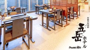 A hotel interior with multiple dining tables and chairs, large windows, and a view of the outside.