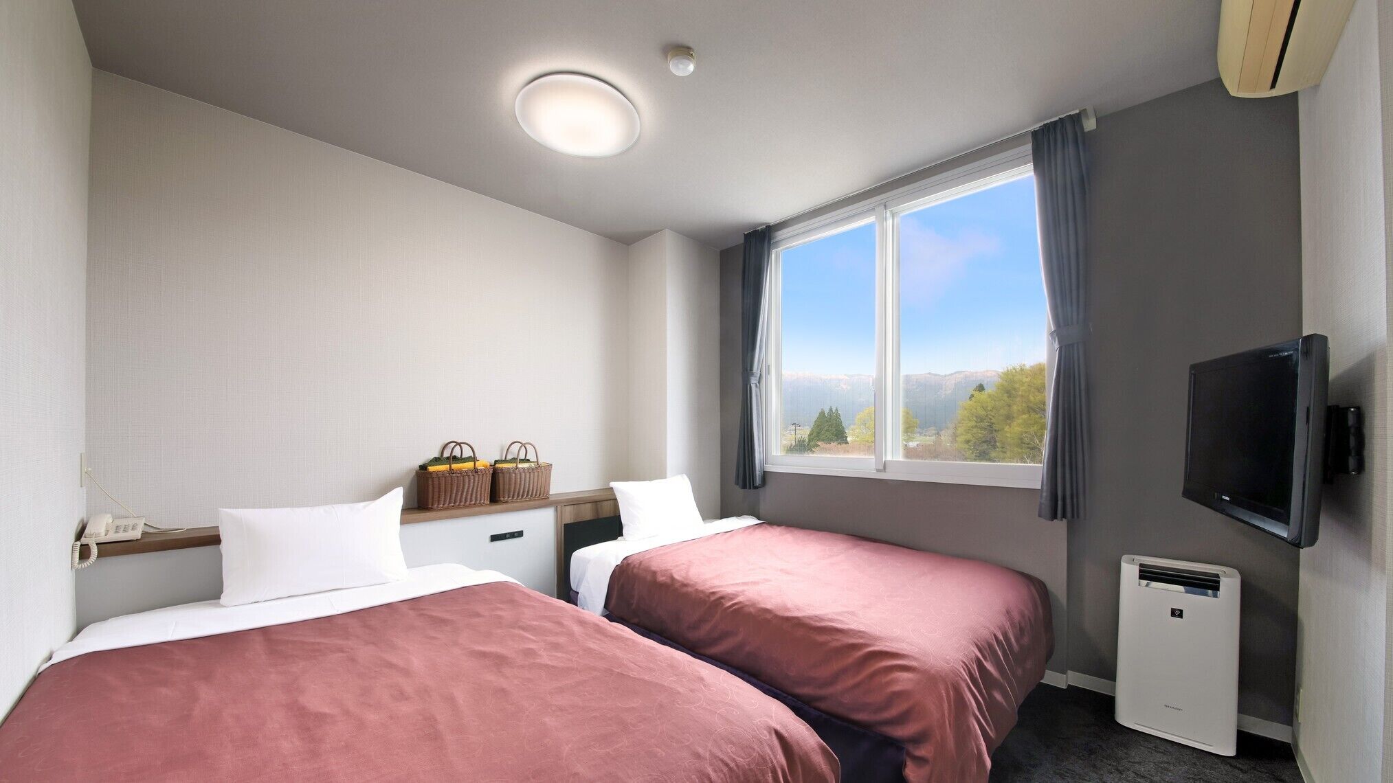 A hotel room with two beds, a TV, a heater, a window with a mountain view, and a phone on the nightstand.