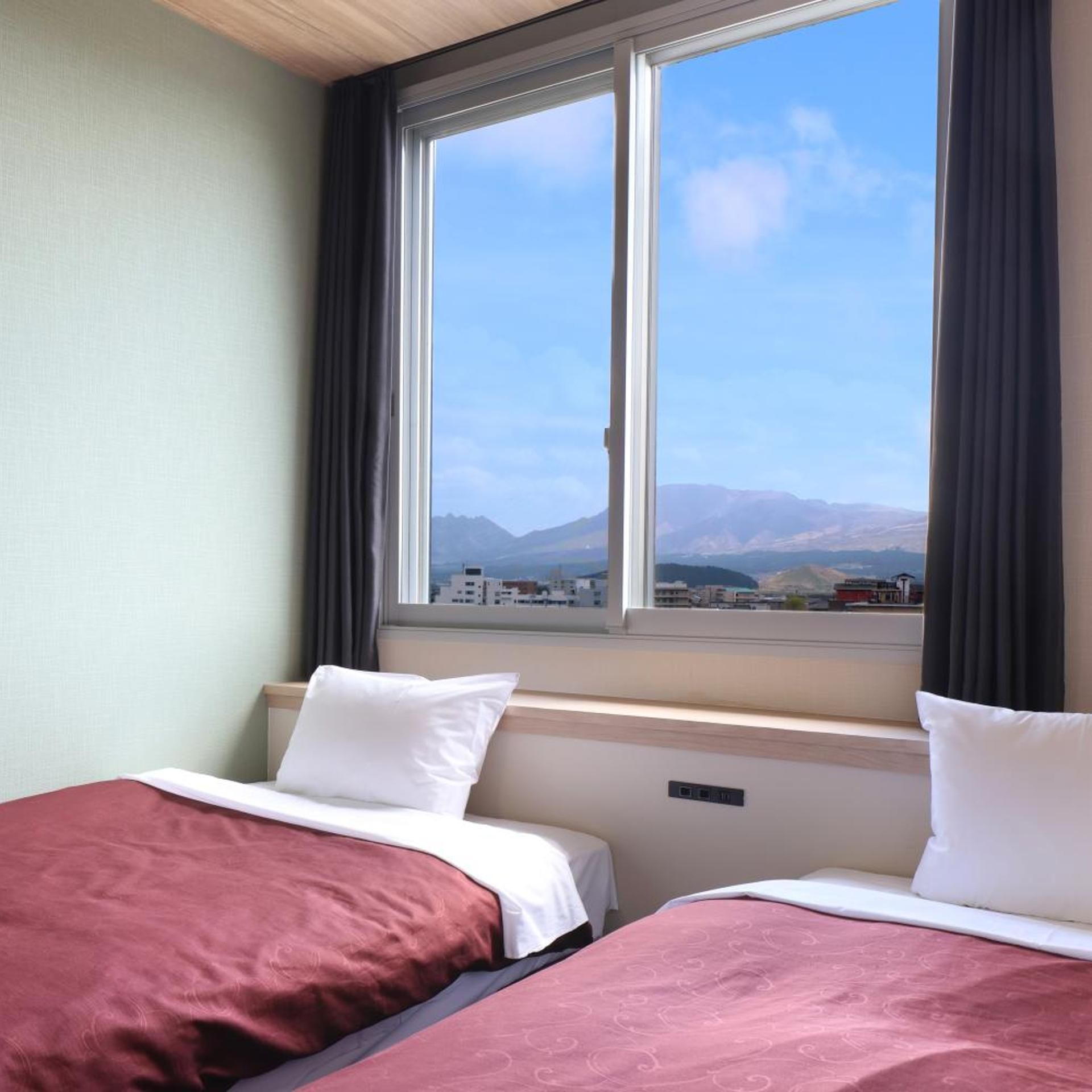 A hotel room with two beds, a large window with a view of mountains, and a cityscape.