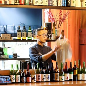 A bar with a variety of bottles, a television in the background, and a person handling a plastic bag. - Aso Uchinomaki Onsen Gogaku Hotel (Aso)