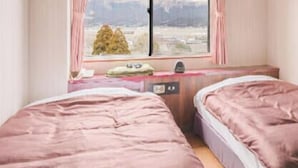 A bedroom with two beds, a desk, and a window with a view of a mountainous landscape.