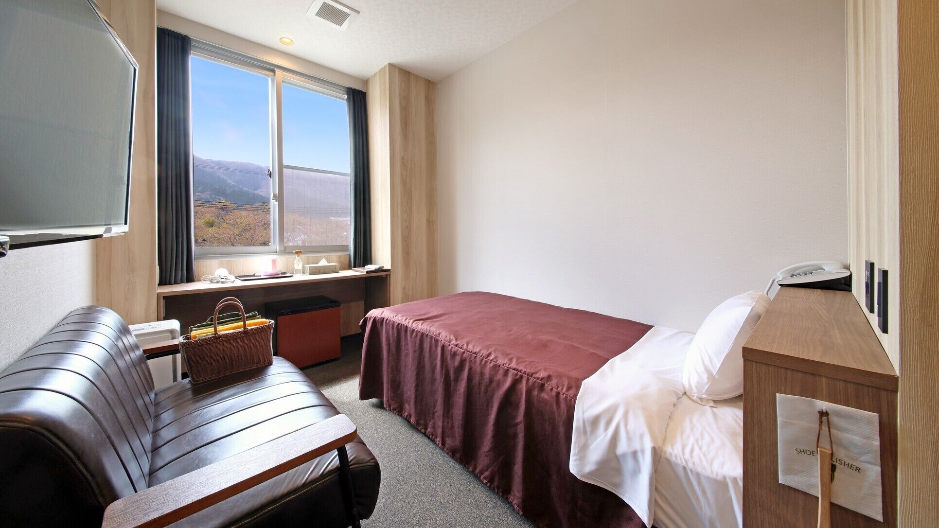A hotel room with a bed, a desk, a chair, a window with a view, and a telephone.
