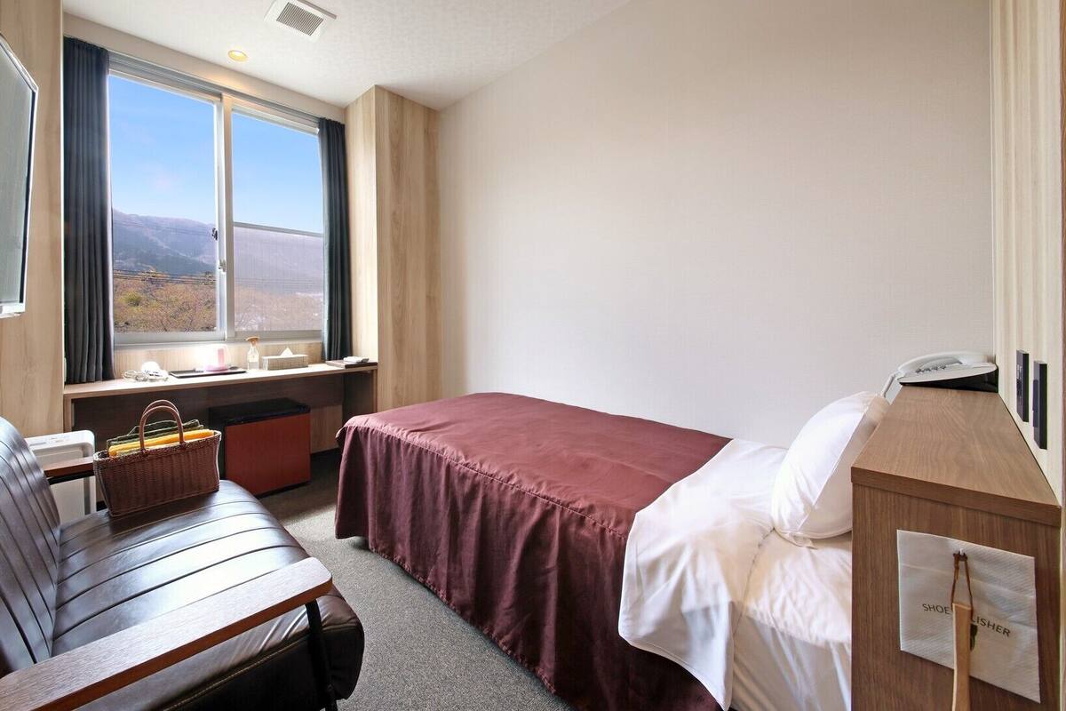 Una habitación de hotel con cama, escritorio, silla, ventana con vistas y teléfono.