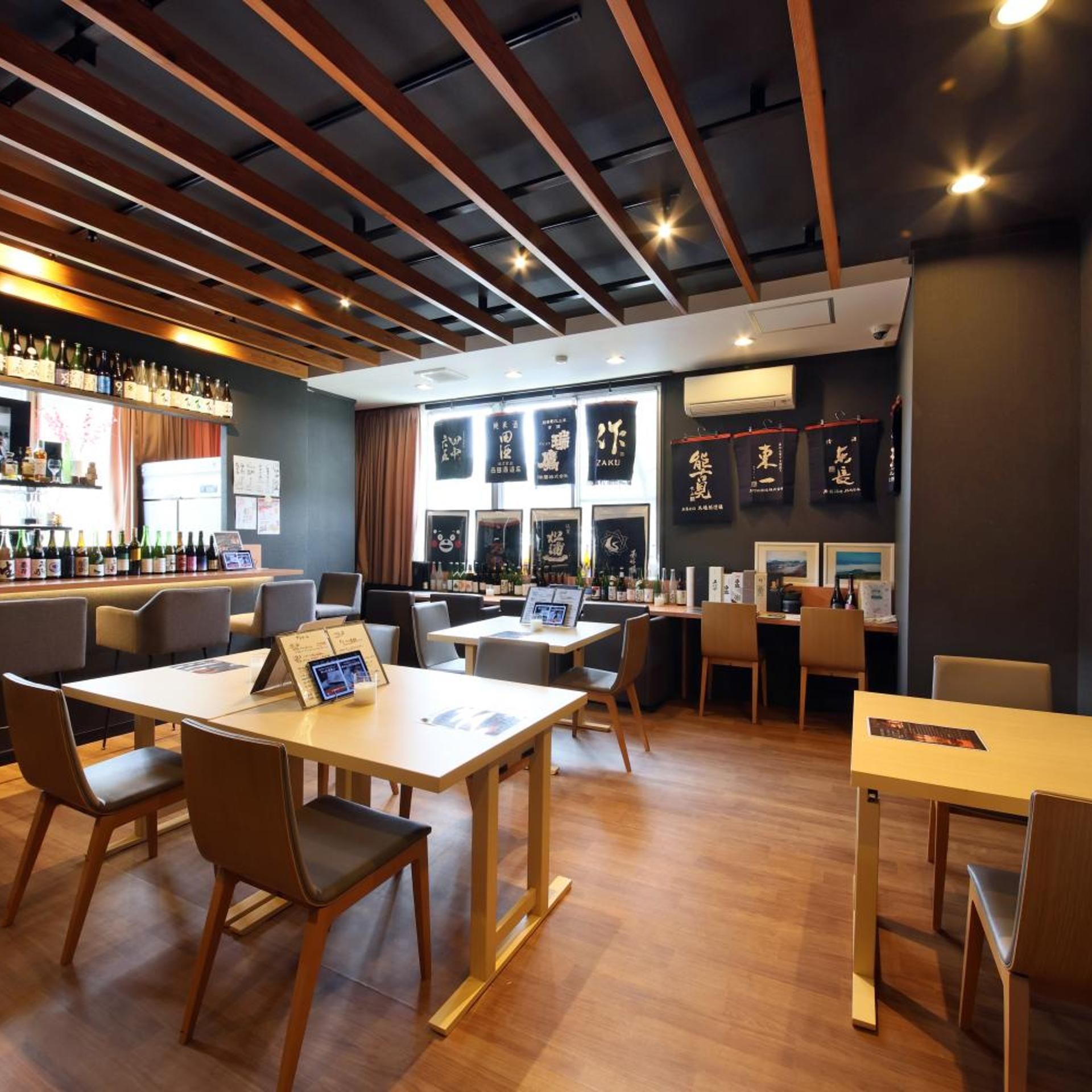 A restaurant interior with wooden tables and chairs, a bar area with bottles, and framed pictures on the walls.