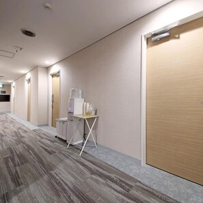 A hotel corridor with a water dispenser, a small table with items, and a door with a number. - Aso Uchinomaki Onsen Gogaku Hotel (Aso)