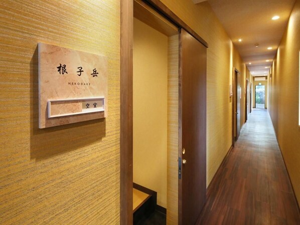 A hotel corridor with a wooden floor, a reception desk, and a door leading to a room. - Aso Uchinomaki Onsen Gogaku Hotel (Aso)