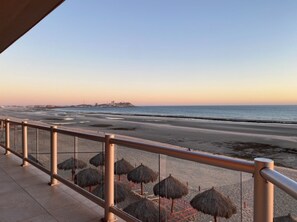 A beach view with a railing, umbrellas, and a distant shoreline.