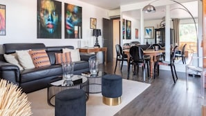 A modern living room with a black leather sofa, a dining area with a wooden table and chairs, and abstract art on the walls. - Les Patios by Interhome (Saint-Tropez)