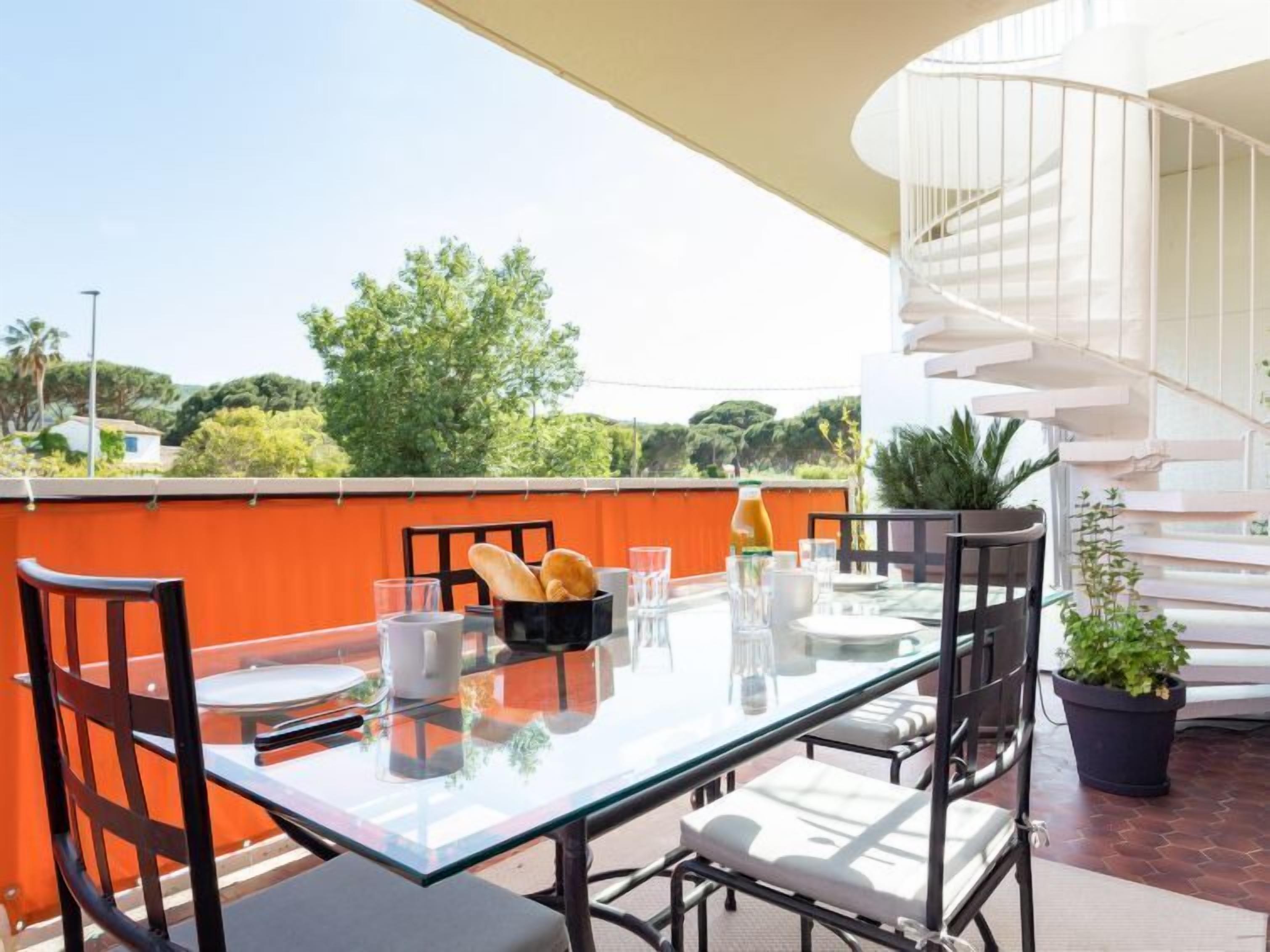 A glass-top dining table with chairs, a spiral staircase, and a view of greenery.