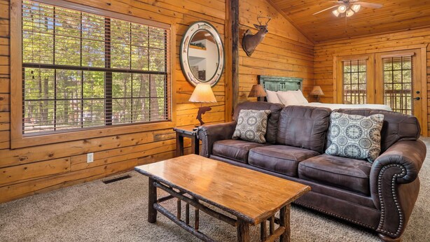 A cozy cabin interior with a leather sofa, a wooden table, a mounted deer head, and a ceiling fan. - Romantic Hideaway Walk-in Cabin for Two - Fireplace & Whirlpool Tub (Branson)