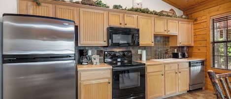 Una cocina con gabinetes de madera, un refrigerador de acero inoxidable, un microondas negro y un horno.