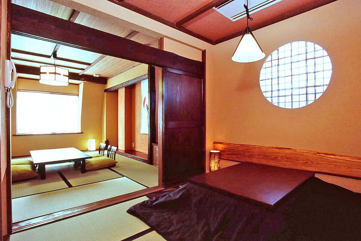 A traditional Japanese room with tatami flooring, a low table, a hanging light fixture, and a circular window.