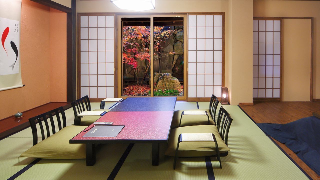 A tatami mat room with a low table, chairs, and a view of a garden through shoji screens.