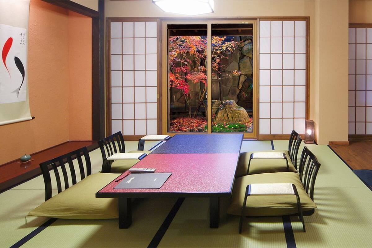 A tatami mat room with a low table, chairs, and a view of a garden through shoji screens.