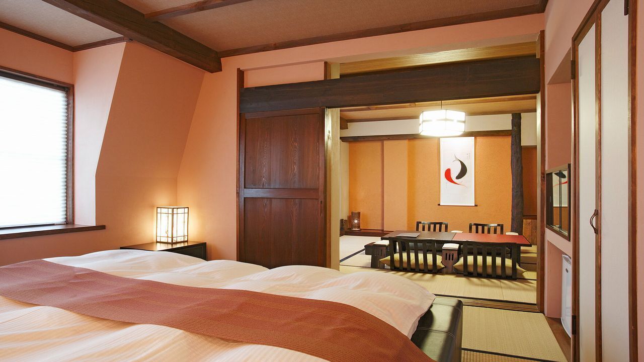 A hotel room with a bed, a desk, a chair, a table, and a mirror.