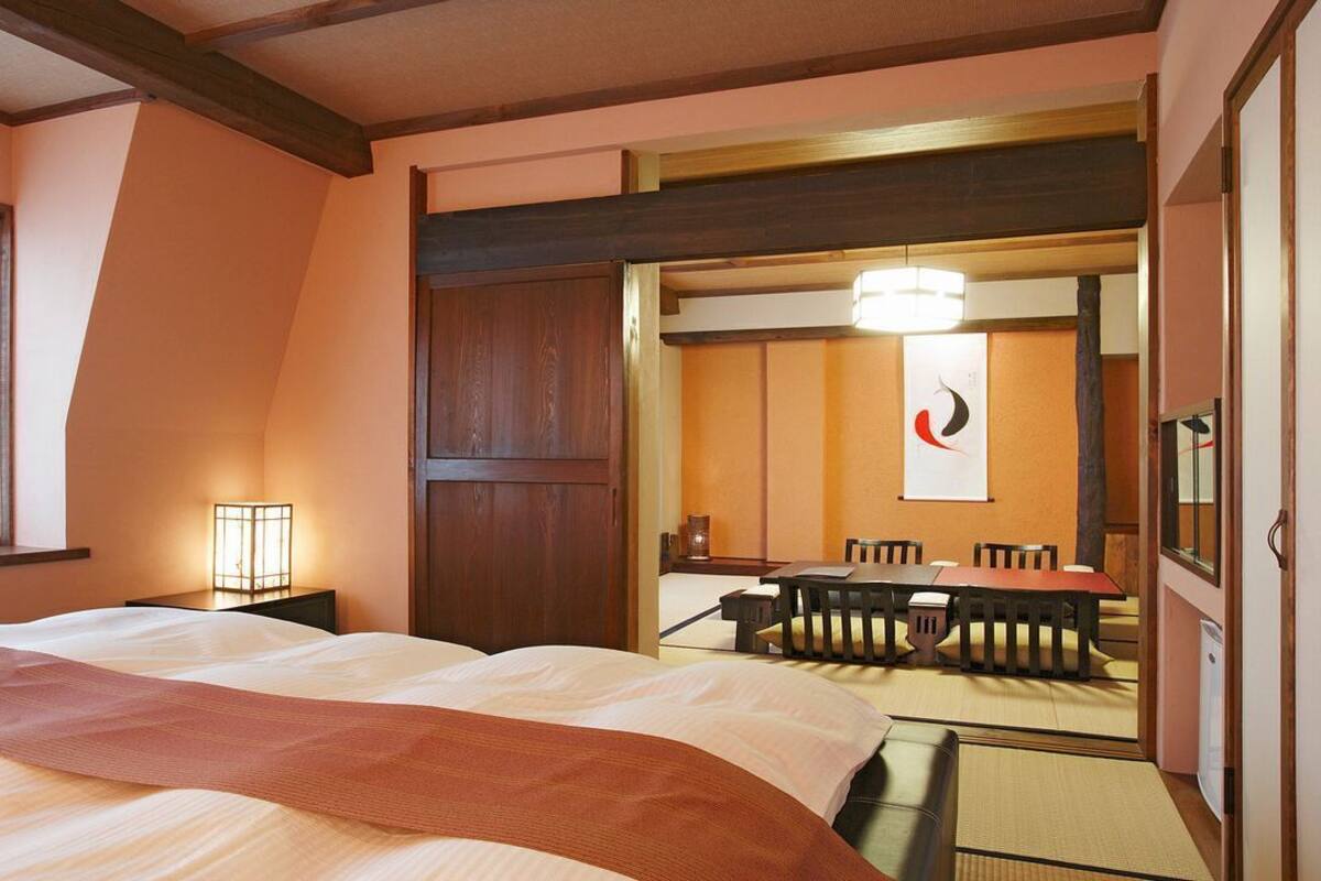 A hotel room with a bed, a desk, a chair, a table, and a mirror.