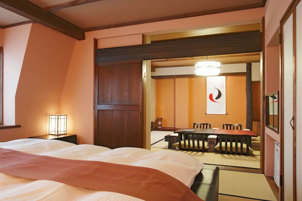 A hotel room with a bed, a desk, a chair, a table, and a mirror.