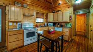 Interior de una cabaña de madera con una cocina que incluye armarios de madera, estufa, microondas y pileta.
