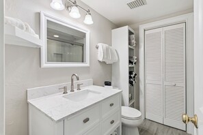 A bathroom with a white vanity, a sink, a mirror, a toilet, and a storage closet with shelves. - East Beach Villa, sleeps 6, near the beach and Dog Friendly, walk to beach (Saint Simons Island)