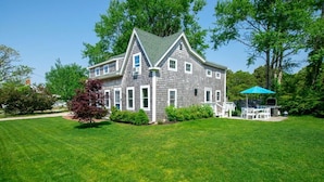 A two-story house with a green roof, white trim, and a front porch with a blue umbrella.