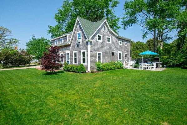 A two-story house with a green roof, white trim, and a front porch with a blue umbrella.