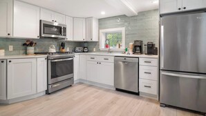 A modern kitchen with white cabinets, stainless steel appliances, and a window overlooking greenery.