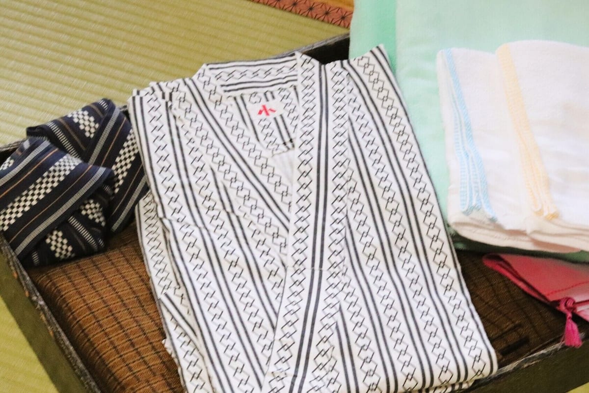 A neatly folded set of clothing including a patterned shirt, a striped shirt, and a folded white garment with a yellow stripe.