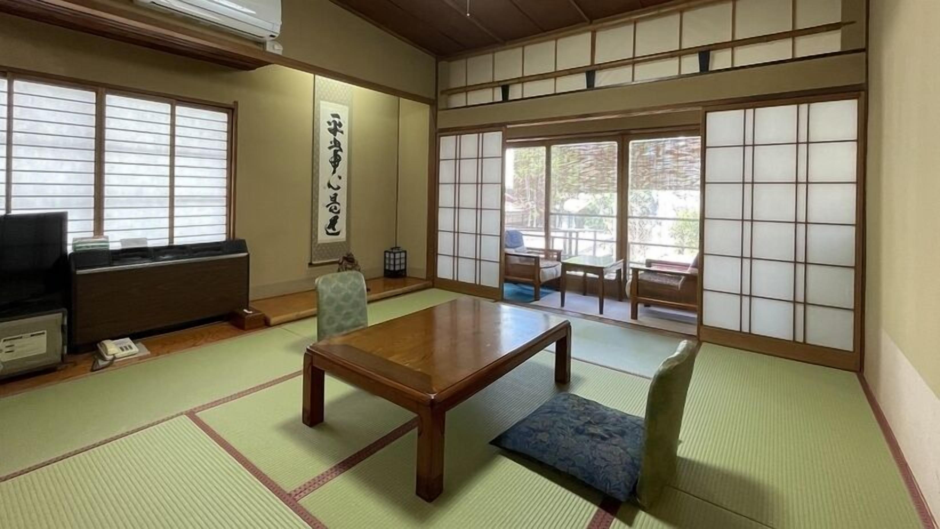 Ein traditioneller japanischer Raum mit Tatami-Böden, einem niedrigen Tisch, einem Stuhl, einem Fernseher und verschiebbaren Türen.