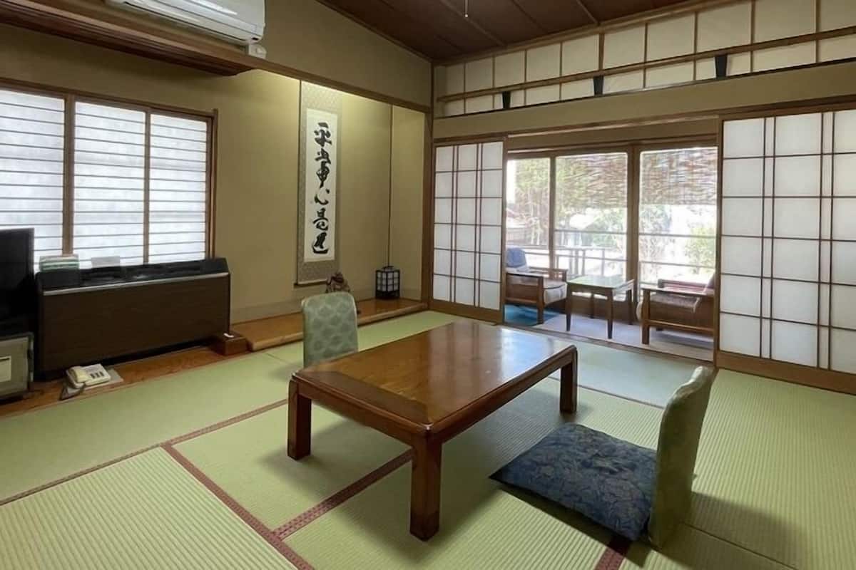 A traditional Japanese room with tatami flooring, a low table, a chair, a TV, and sliding doors.