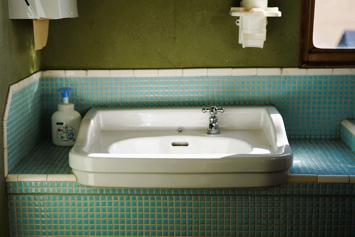 A bathroom with a white sink, blue-tiled walls, a bottle of soap, and a towel dispenser.