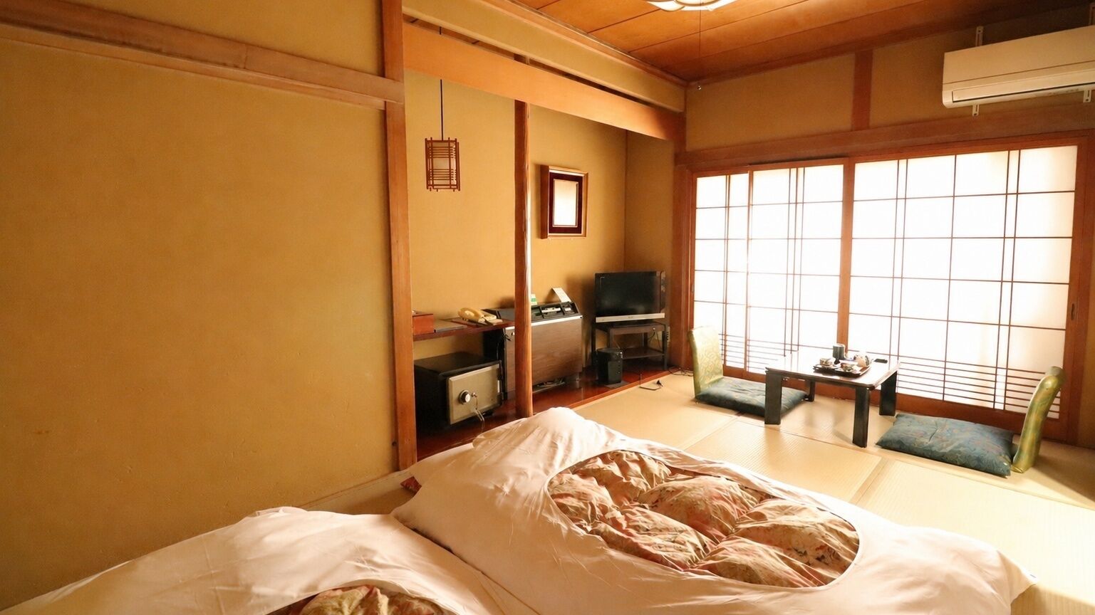Ein traditioneller japanischer Raum mit Tatami-Böden, einem Futonbett, einem Fernseher und einer Schiebetür.