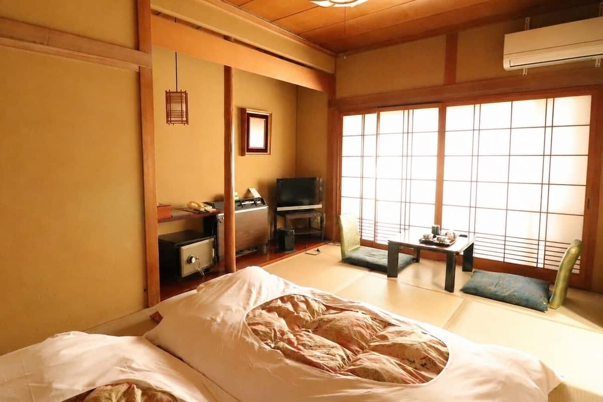 A traditional Japanese room with tatami flooring, a futon bed, a television, and a sliding door.