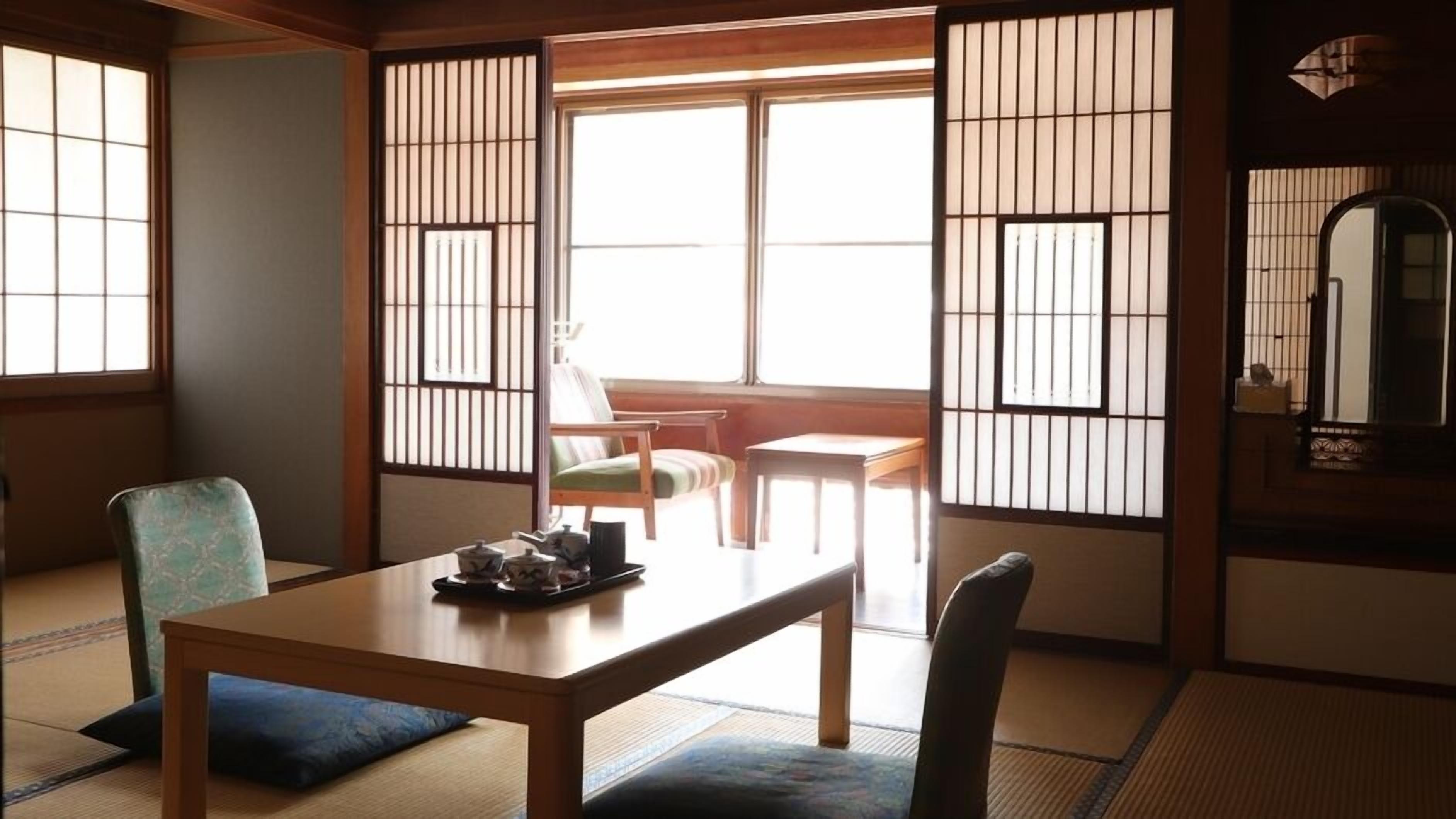 Ein traditioneller japanischer Raum mit Tatami-Bodenbelag, einem niedrigen Tisch mit Teeset und verschiebbaren Shoji-Schiebetüren.