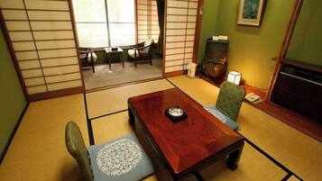 A tatami mat room with a low wooden table, two chairs, a television, and a framed picture on the wall.