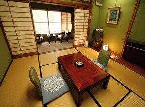 A tatami mat room with a low wooden table, two chairs, a television, and a framed picture on the wall.