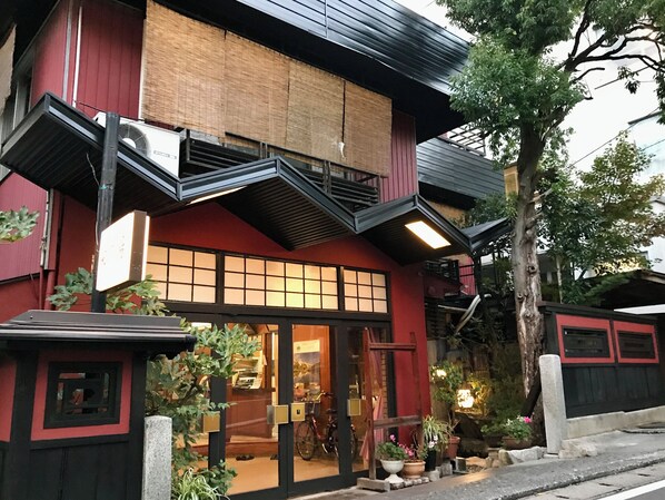 A building with a red facade, a wooden balcony, and a storefront with glass doors.