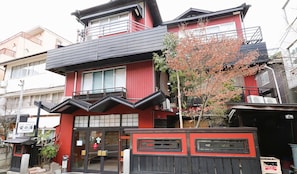 Un edificio de varios pisos con fachada roja, un balcón y la entrada a una pequeña tienda.