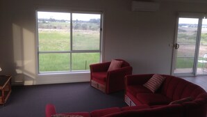 A living room with a red sofa set, a wooden coffee table, and a large window offering a view of a grassy field. - Cottage Down the Lane Rural Setting (Meredith)