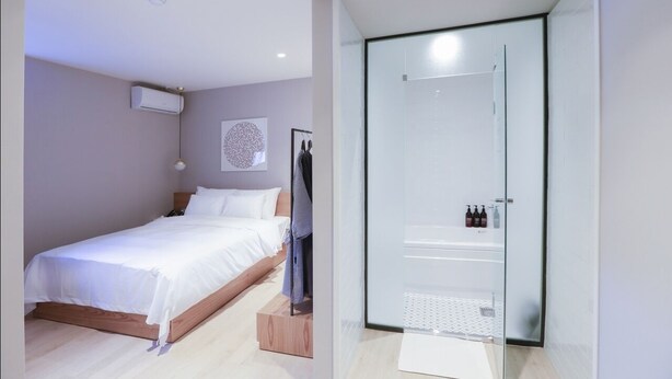 Une chambre à coucher moderne avec un lit en bois, une cabine de douche en verre et un climatiseur fixé au mur.