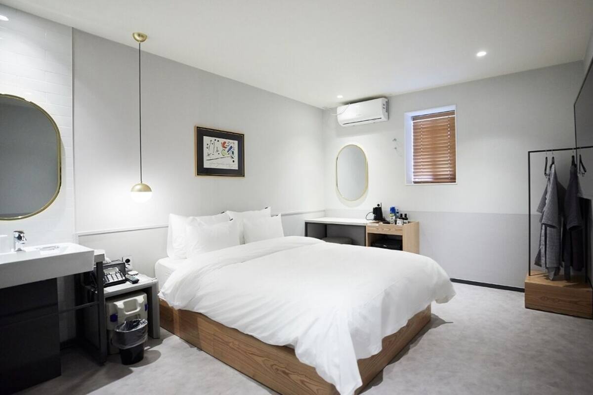 Une chambre moderne avec un grand lit, une table de chevet, une coiffeuse avec un miroir et un téléviseur fixé au mur.